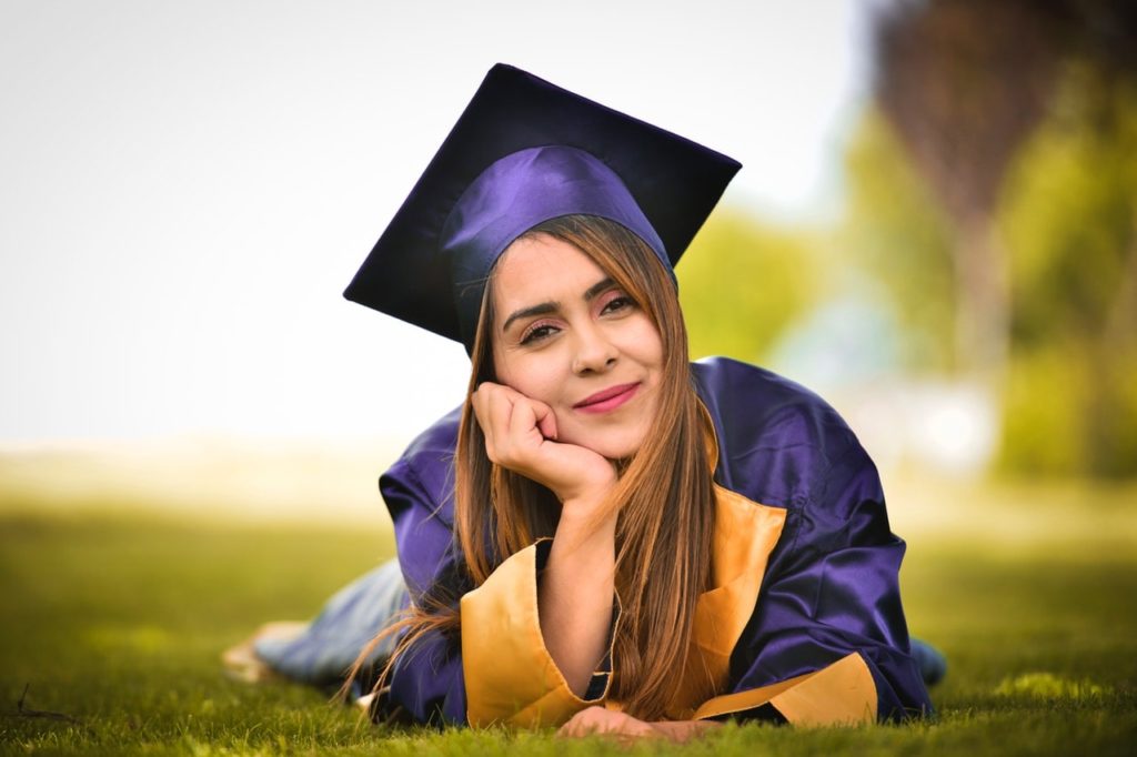Woman wearing purple graduation gown lying on grass